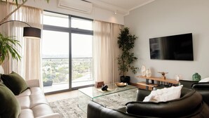 A modern living room with a glass coffee table, a sofa, a large potted plant, and a flat-screen TV mounted on the wall.