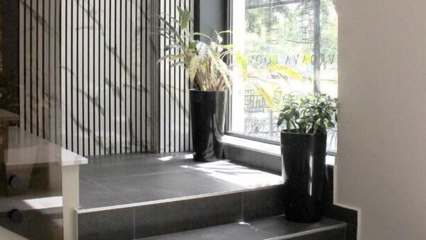 Un intérieur moderne avec un escalier menant à une fenêtre, une plante en pot et un mur à rayures verticales.
