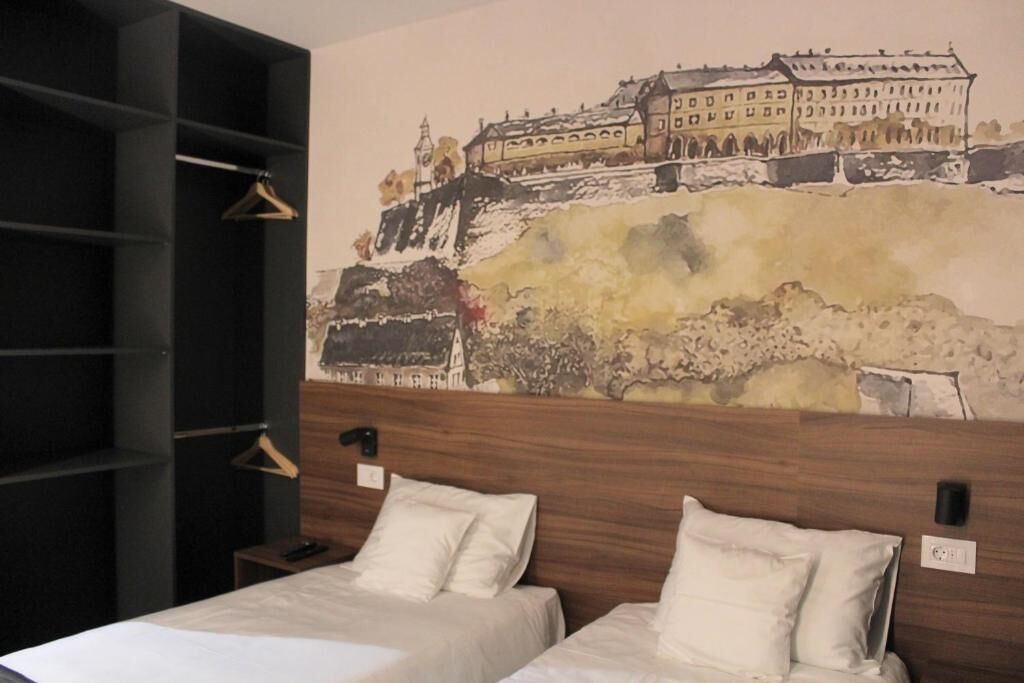 A hotel room with two beds, a wooden headboard, and a large wall mural of a historic building.