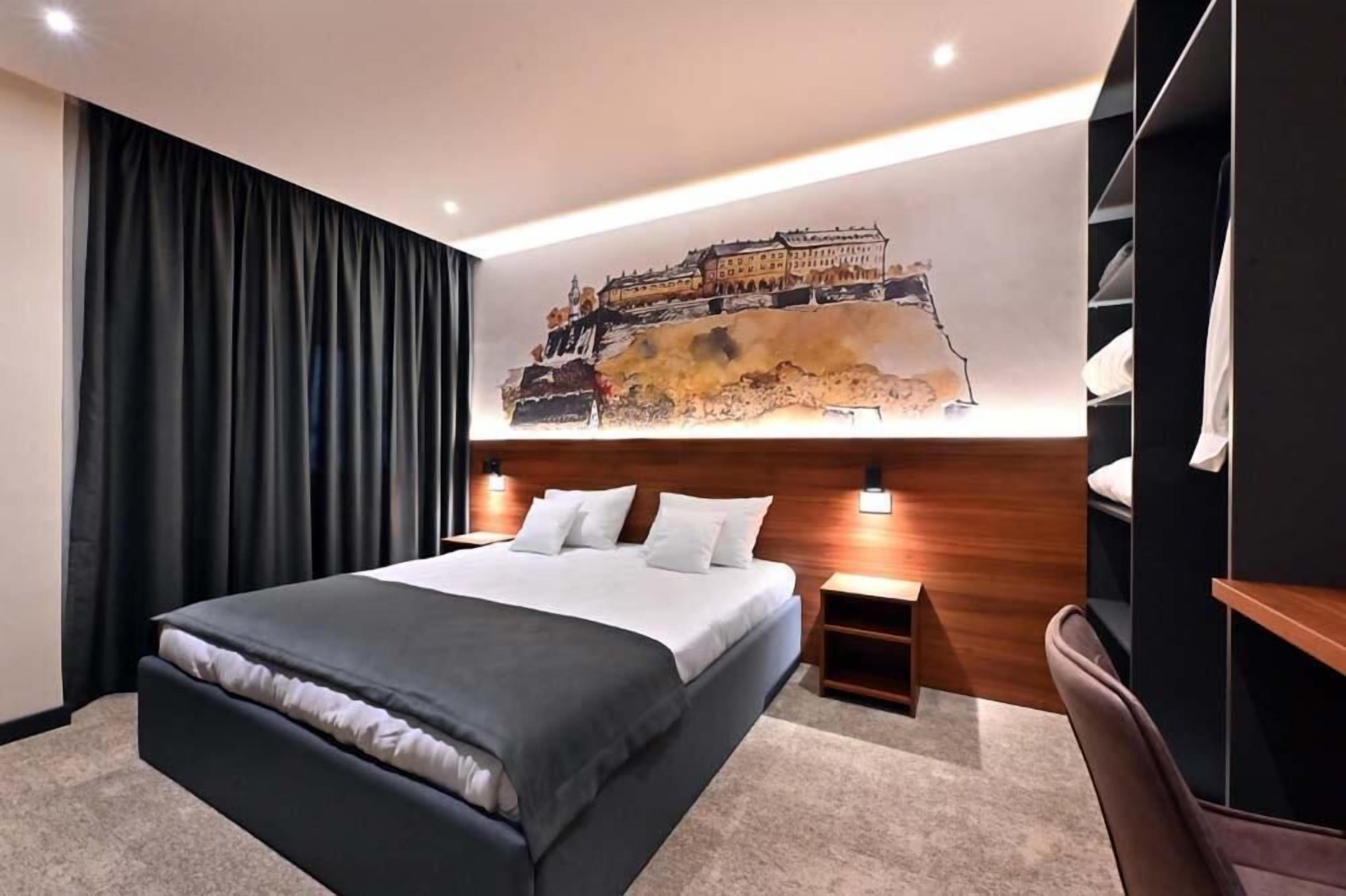 Una habitación de hotel moderna con una cama grande, cabecera de madera, mesita de noche, escritorio y un mural grande en la pared.