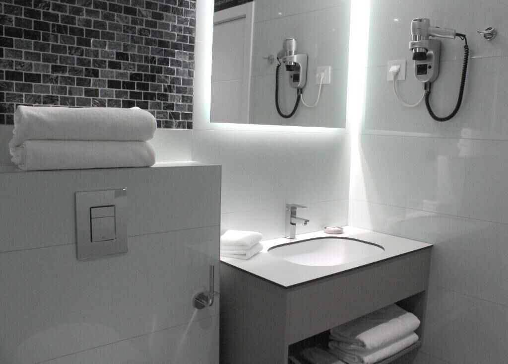 A modern bathroom with a white sink, a towel rack, and a hairdryer mounted on the wall.