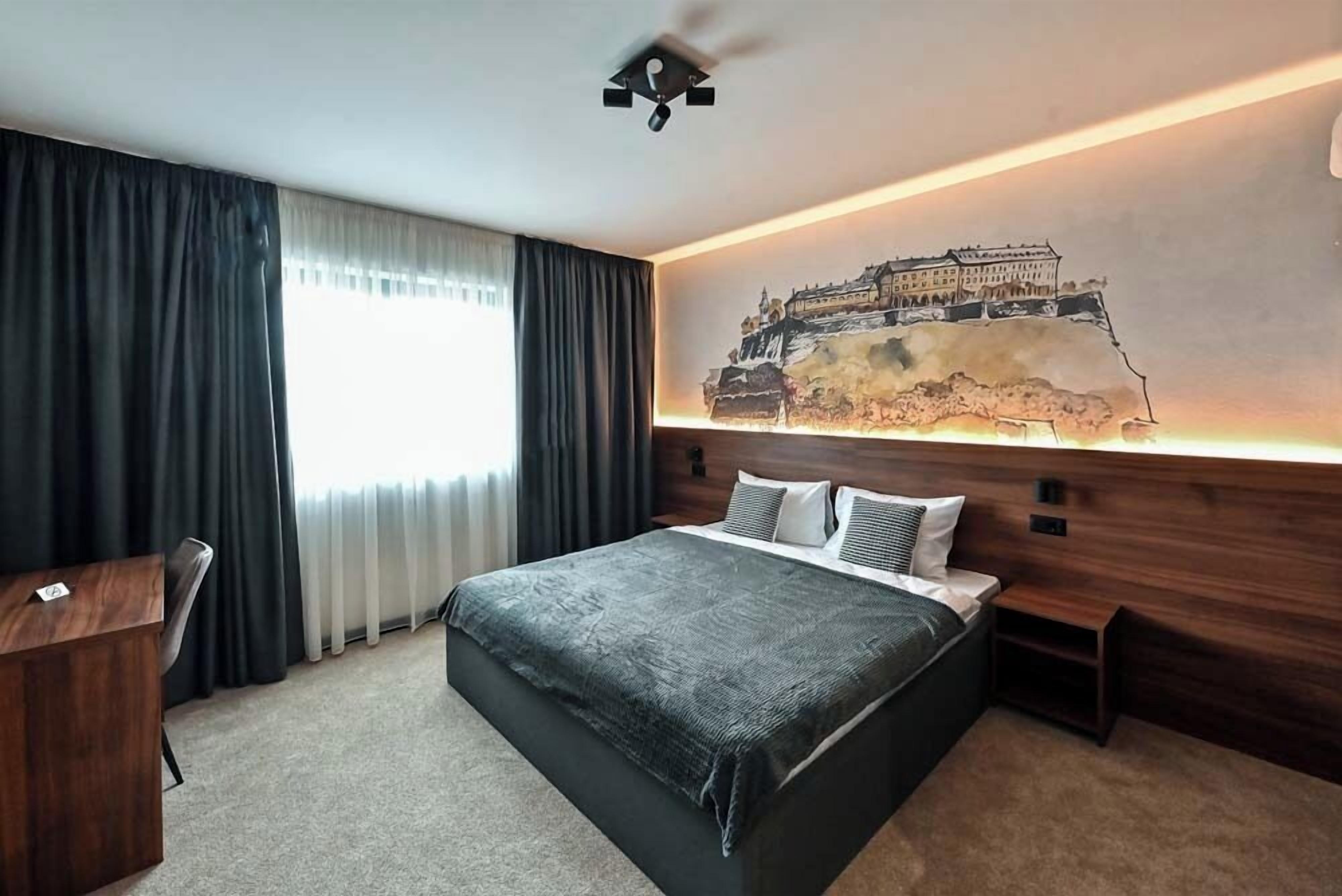 Ett modernt hotellrum med en stor säng, ett skrivbord och en tavla som föreställer ett slott, upphängd på väggen.