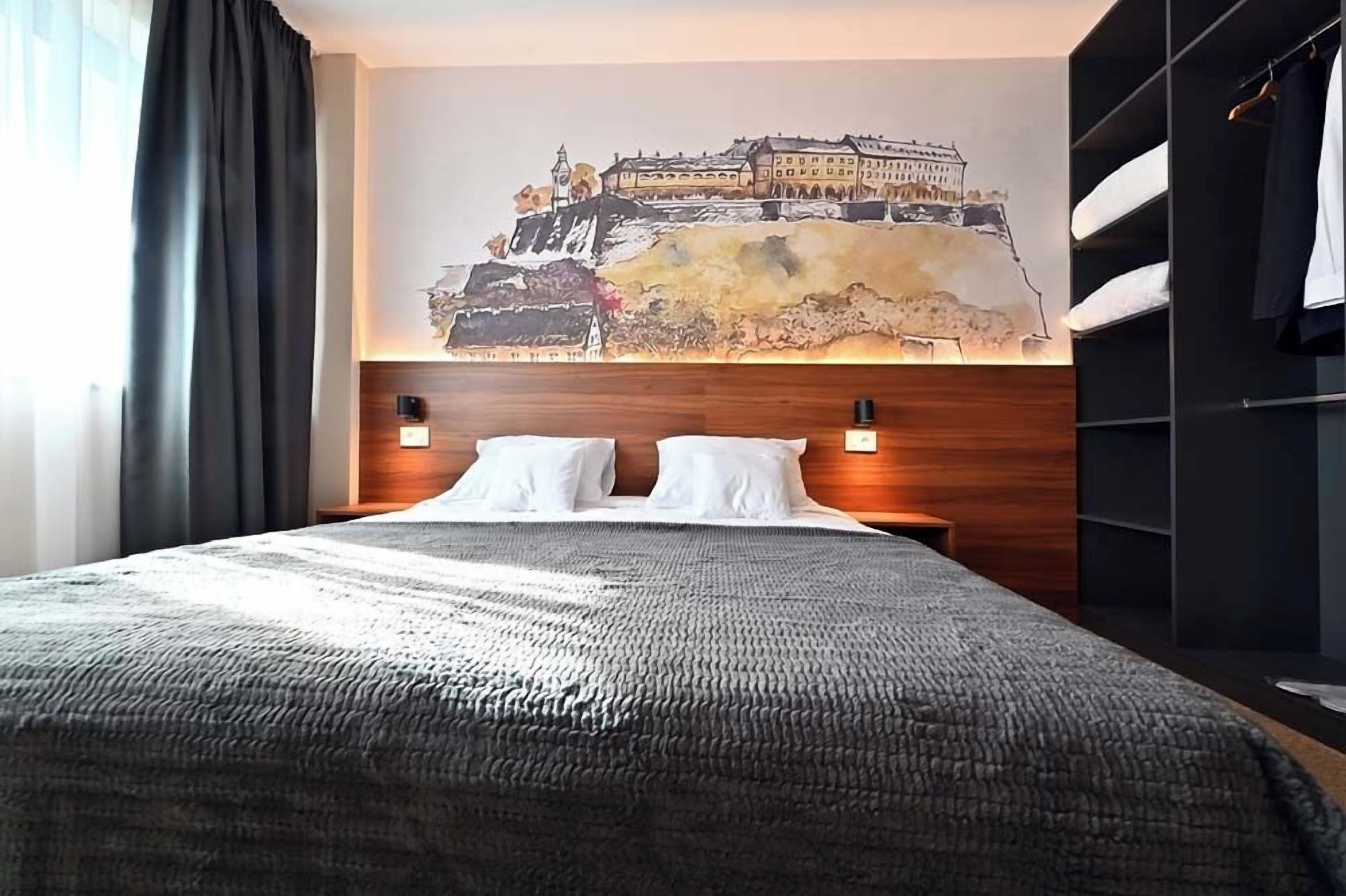 A hotel room with a large bed, two bedside tables with lamps, a wardrobe, and a wall mural.
