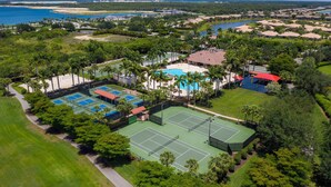 An aerial view of a resort with multiple tennis courts, a swimming pool, and a beachfront.