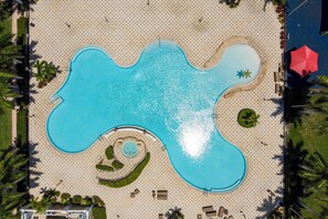 Vista aérea de una zona de piscina con forma singular, rodeada por un suelo con diseño, palmeras y sillas de descanso.