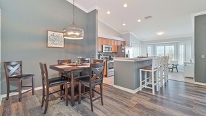 A spacious dining area with a wooden table and chairs, a kitchen with modern appliances, and a large window providing natural light.