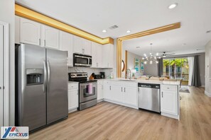 A modern kitchen with white cabinets, stainless steel appliances, and a wooden floor.