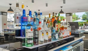 Un bar con varias botellas de licor, incluyendo Bacardi y Captain Morgan, y una computadora portátil sobre la barra.