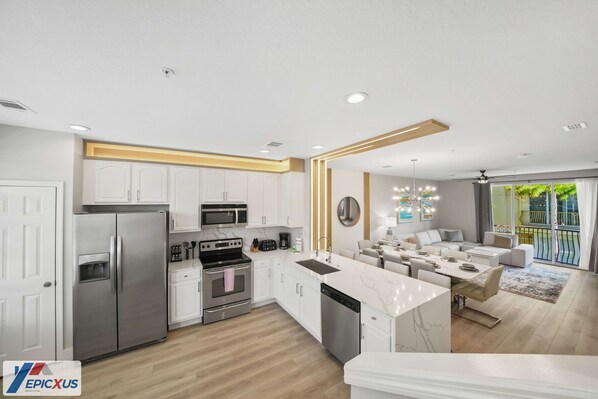 A modern kitchen with white cabinetry, stainless steel appliances, and a marble island.