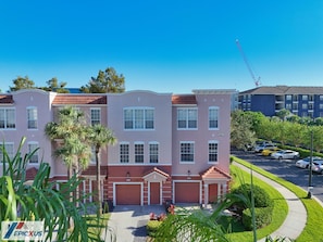 Un edificio residencial de varios pisos con fachada roja y rosa, múltiples puertas de garaje y un estacionamiento con varios coches.