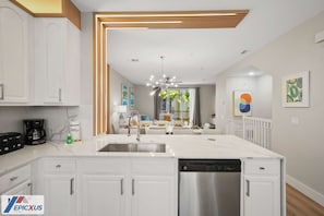 A modern kitchen with white cabinetry, a stainless steel dishwasher, and a central island with a sink.