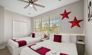 A hotel room with two beds, a ceiling fan, a window with blinds, and two red star decorations on the wall.