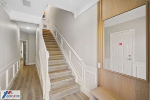 Una escalera con barandas blancas y peldaños de madera que conduce a una puerta con una etiqueta roja.