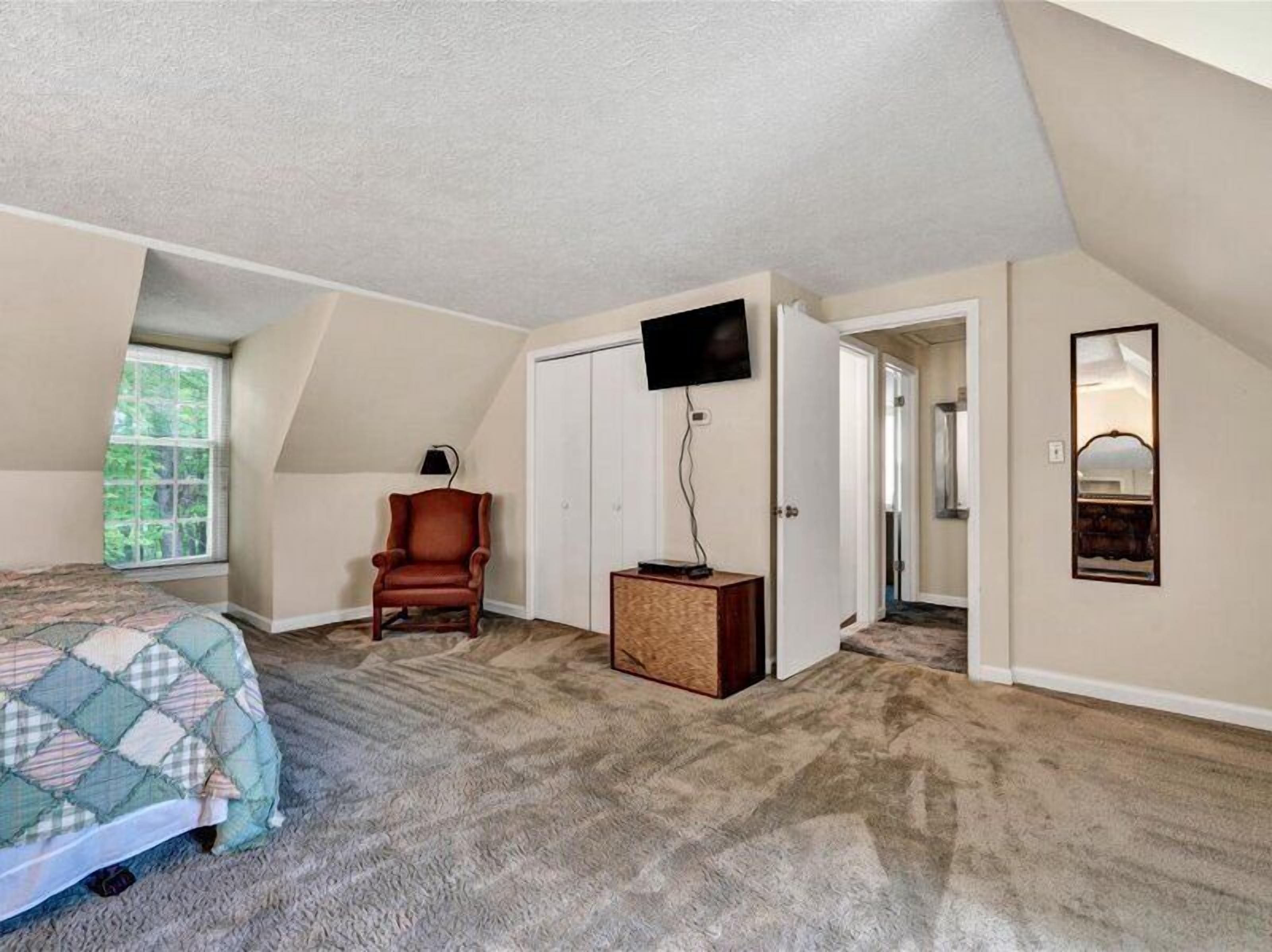 A bedroom with a bed, a chair, a TV, a wardrobe, and a mirror.