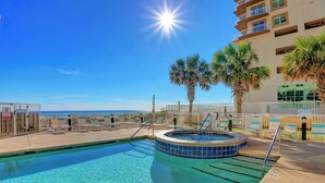 A pool area with a hot tub, palm trees, and a view of the ocean.