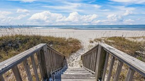 A wooden staircase leading to a beach with a clear view of the ocean and clouds in the sky.