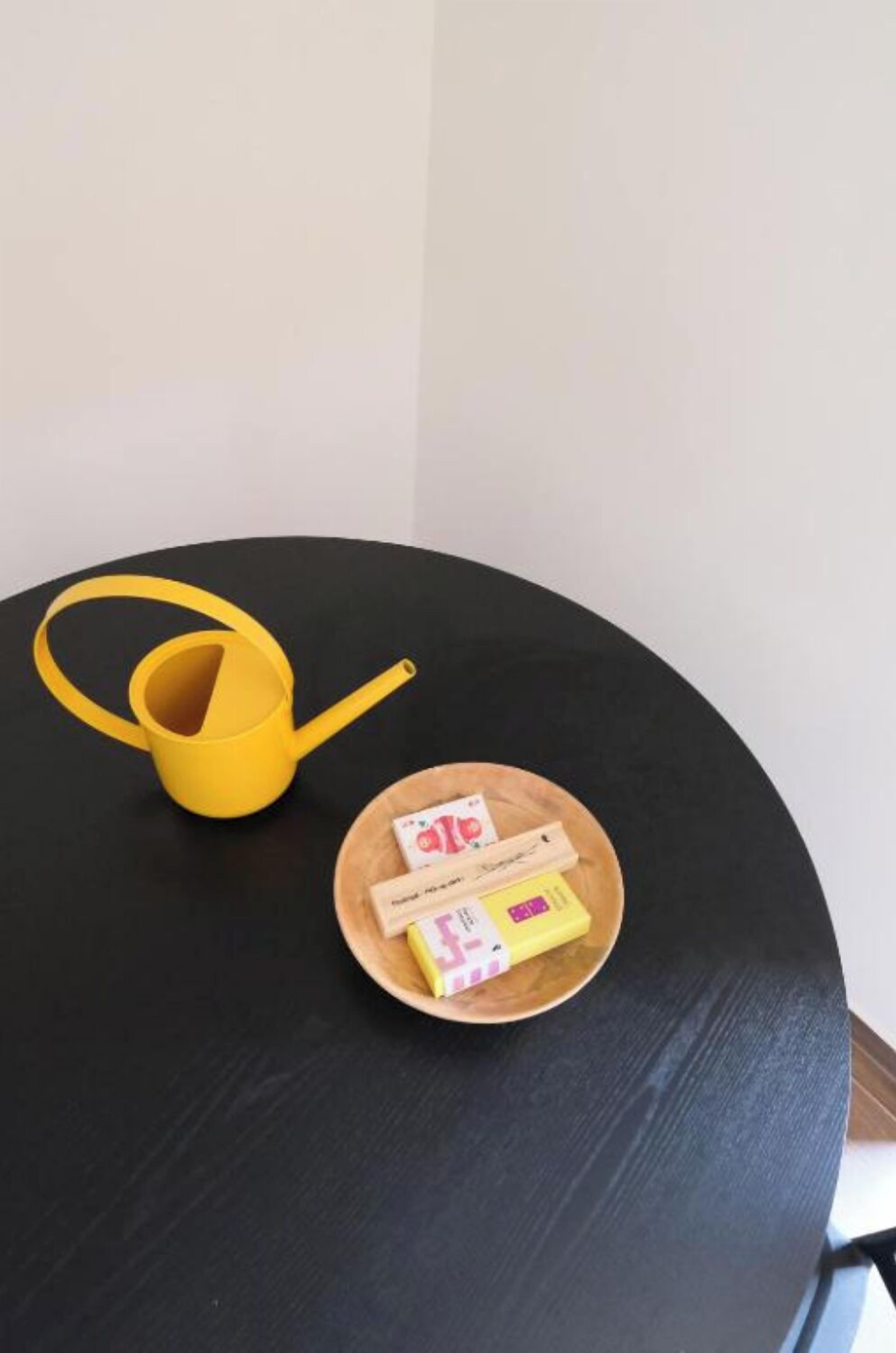 Una mesa redonda negra con un regador amarillo y una bandeja de madera que sostiene dos cajas de pañuelos.