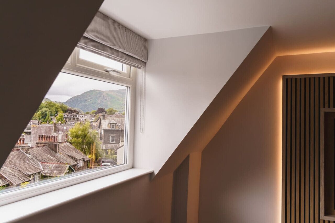 A room with a sloped ceiling, a window with a view of a town and mountains, and a wooden panel wall.