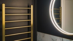 Un bagno con una parete nera, un porta asciugamani dorato e uno specchio rotondo con illuminazione.