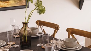 Un tavolo da pranzo apparecchiato con bicchieri trasparenti, un vaso con steli verdi e un quadro incorniciato appeso al muro.