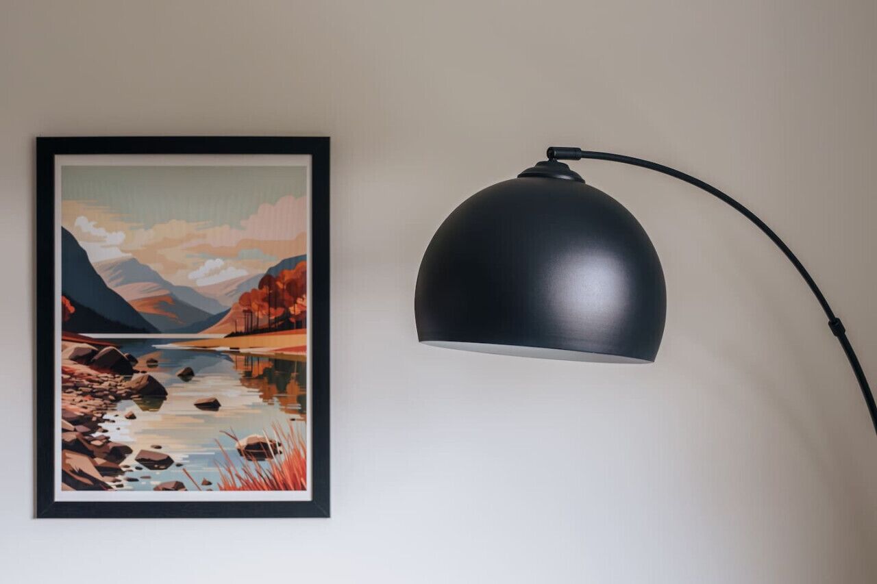 Uma pintura de paisagem emoldurada e uma luminária de mesa preta na parede.