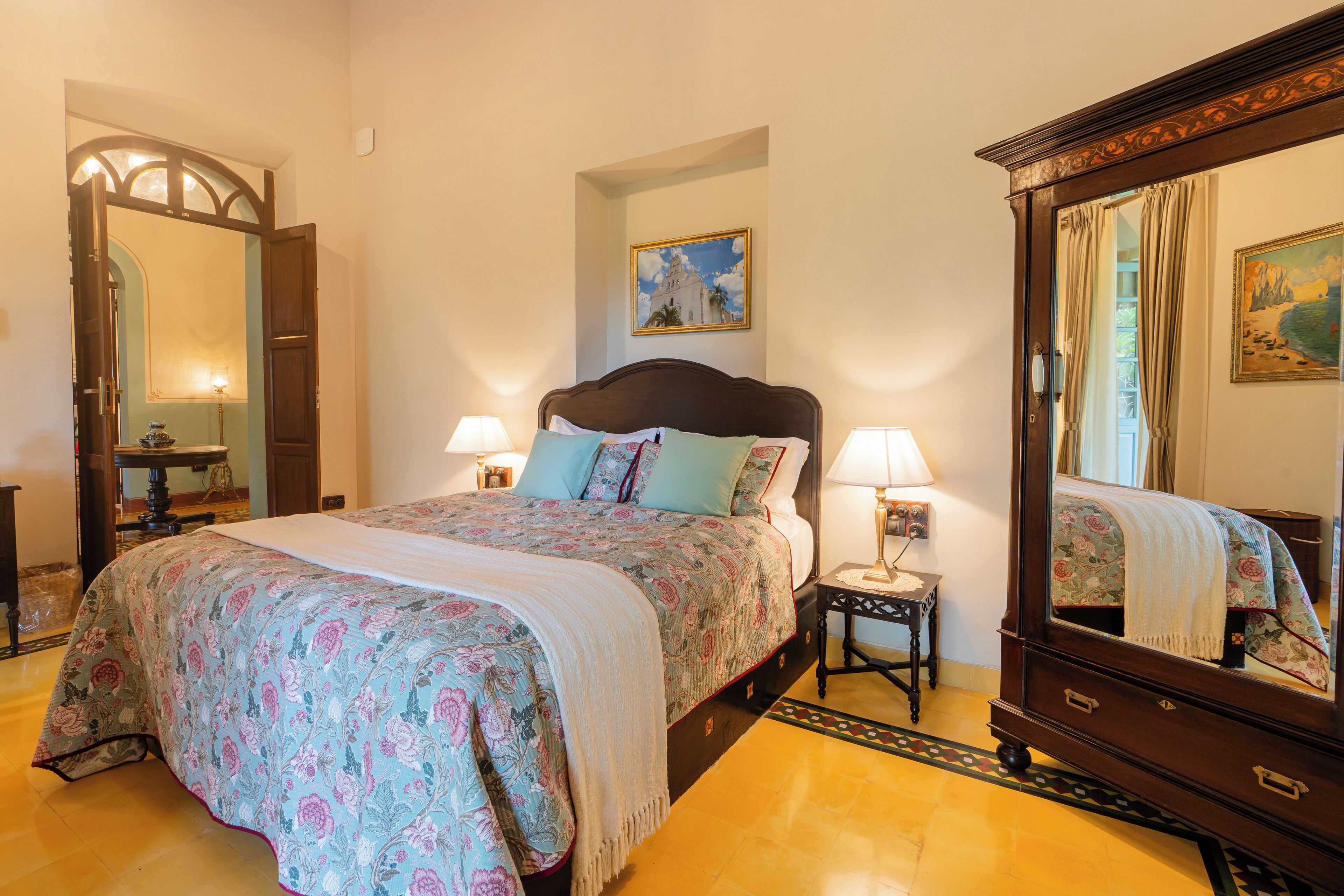 A bedroom with a large bed, two bedside tables with lamps, a mirror, and a painting on the wall.