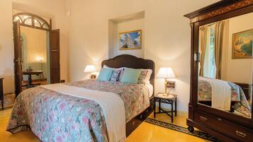 A bedroom with a large bed, two bedside tables with lamps, a mirror, and a painting on the wall.