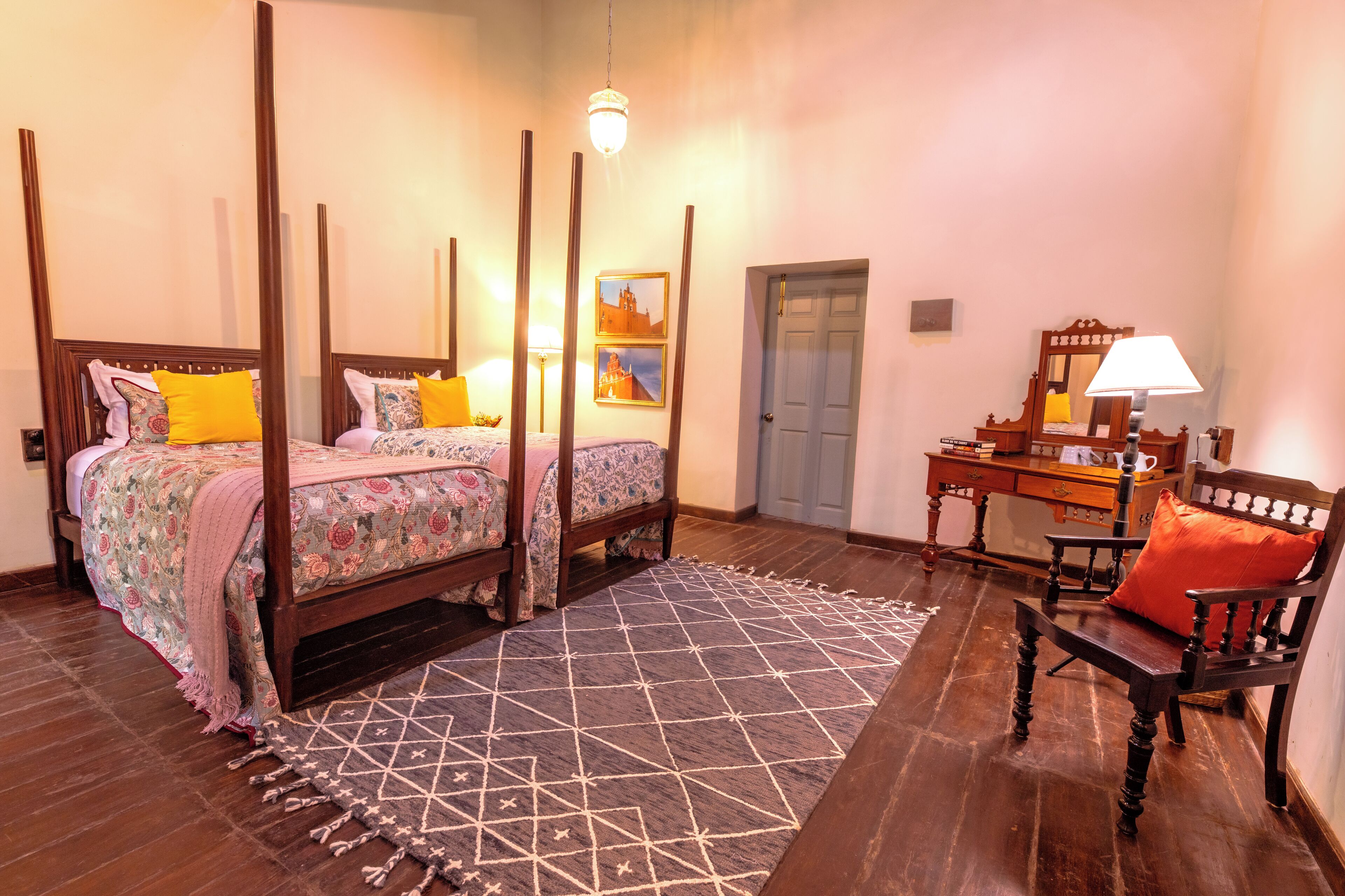 A bedroom with a four-poster bed, a desk with a chair, a patterned rug, and a door.