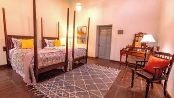 A bedroom with a four-poster bed, a desk with a chair, a patterned rug, and a door.