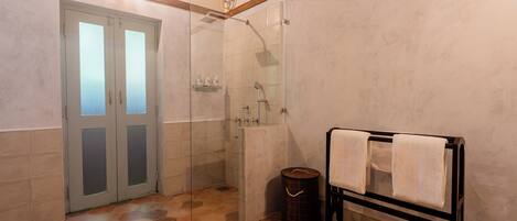 A bathroom with a glass shower enclosure, a towel rack, and a waste bin.