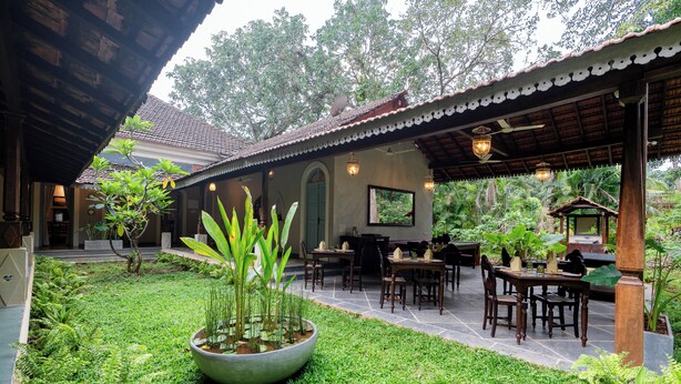 Un patio con zona de comedor, una jardinera grande con plantas y un edificio con tejado de baldosas.