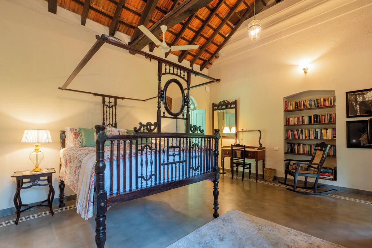 Een slaapkamer met een hemelbed, een bureau, een schommelstoel en een boekenkast.