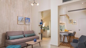 A modern living room with a sofa, coffee table, and ottoman. There is a kitchen area with bar stools and a dining table. - Tatianas Kanevaro (Chania)