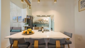 A modern dining area with a large white table, grey upholstered chairs, and a central island with a fruit bowl. - Tatianas Kanevaro (Chania)