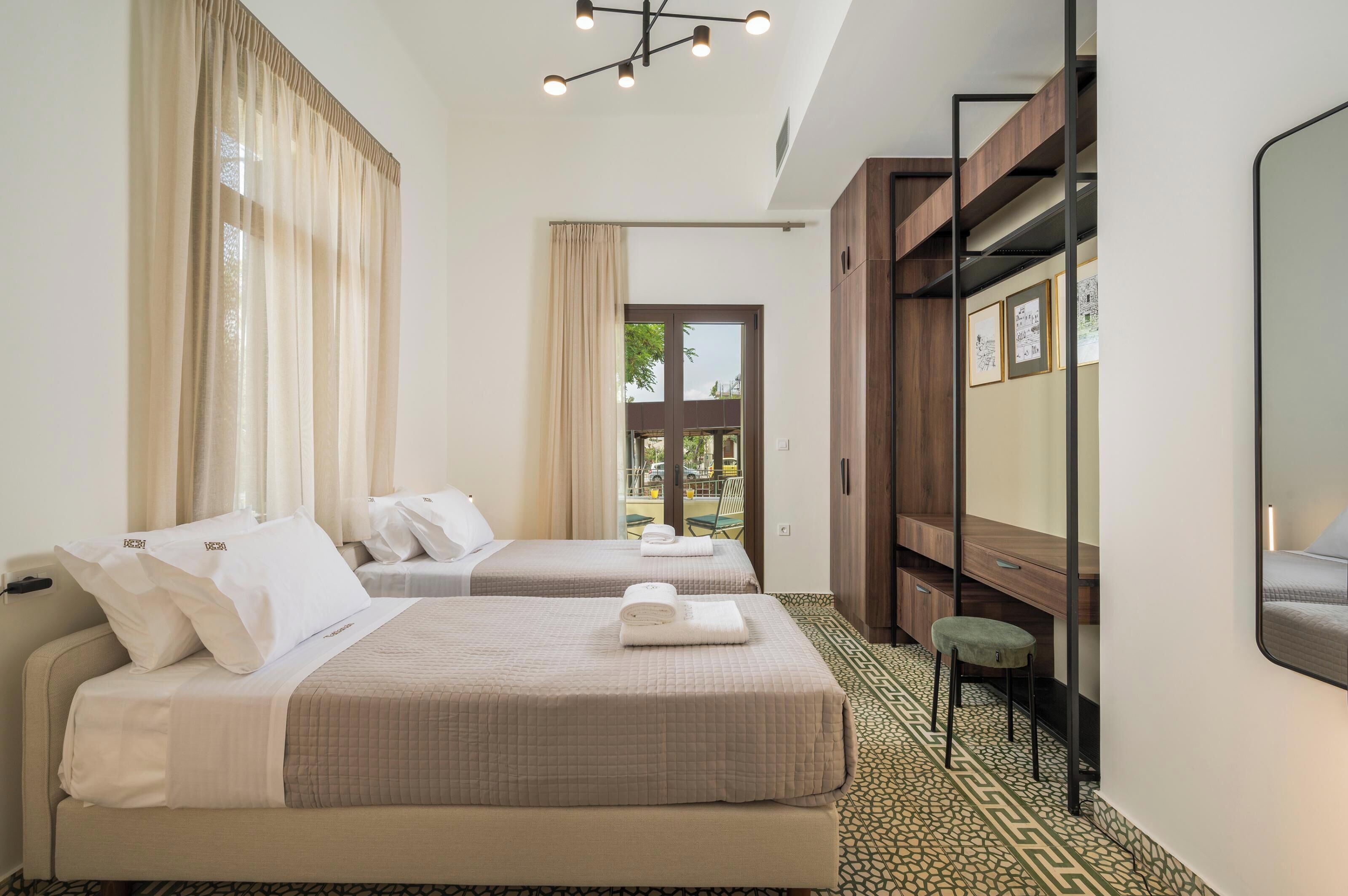 A hotel room with two beds, a desk, a chair, a mirror, and a view of the outdoors.