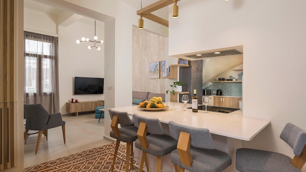 A modern living room with a large TV, a dining area with a white table and grey chairs, and a kitchen with a stainless steel refrigerator. - Tatianas Kanevaro (Chania)