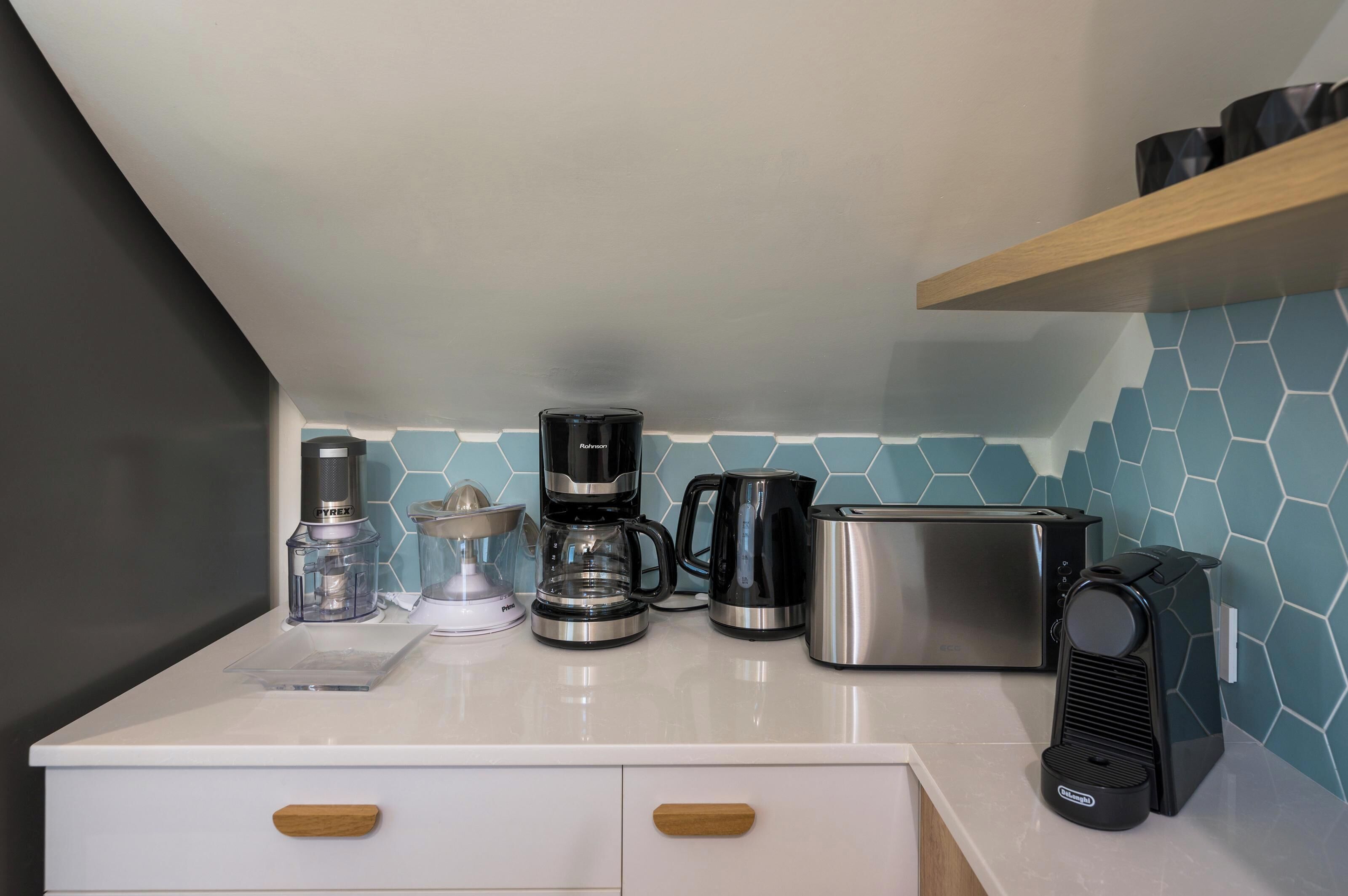 Eine Küche mit weißer Arbeitsplatte, einem Toaster, einer Kaffeemaschine, einem Mixer und einem Wasserkocher.