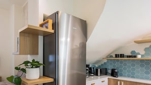 A modern kitchen with a stainless steel refrigerator, wooden shelves, a potted plant, and a hexagonal tile backsplash. - Tatianas Kanevaro (Chania)