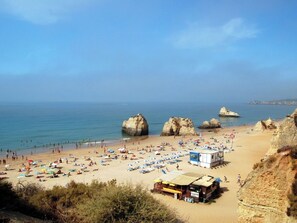 Una playa con grandes formaciones rocosas, una orilla arenosa y varias sombrillas.