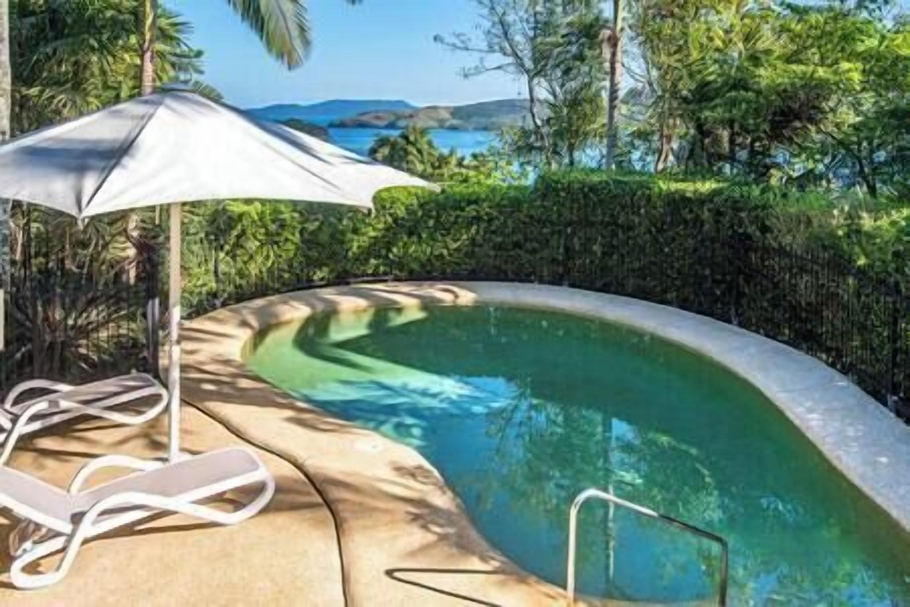 A swimming pool with a curved edge, a white umbrella, and a poolside chair.