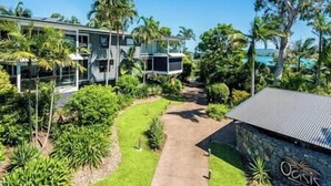 Uma casa moderna de dois andares com uma varanda de vidro ampla, cercada por vegetação exuberante e um céu azul límpido.