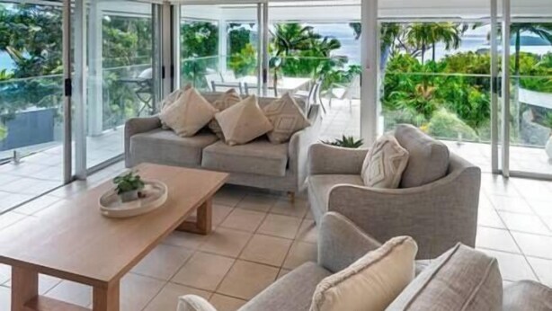 Uma sala de estar moderna com um sofá e poltronas, uma mesa de centro e vista para o exterior.