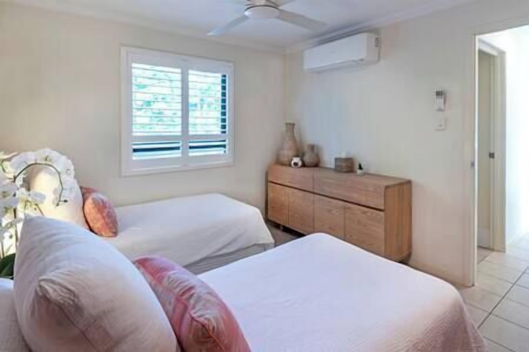 A bedroom with two beds, a wooden dresser, and a window with blinds.