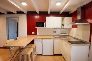Eine kompakte Küche mit Mikrowelle, Herd, Spüle und einem kleinen Kühlschrank. Ein Holztisch und Stühle stehen bereit, und eine Tür führt in einen weiteren Raum.