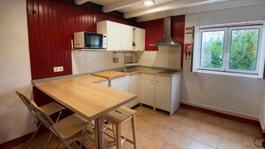 Una cocina compacta con una mesa y sillas de madera, armarios blancos, un microondas y una ventana con vistas a zonas verdes.