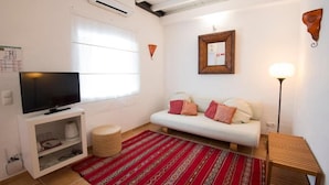 Una sala de estar con televisor, sofá, alfombra roja estampada y una lámpara.