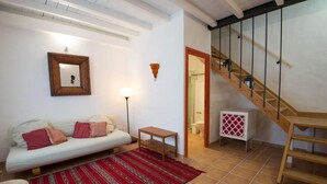 Una sala de estar con un sofá, un tapete estampado, una mesita, un espejo y una escalera.