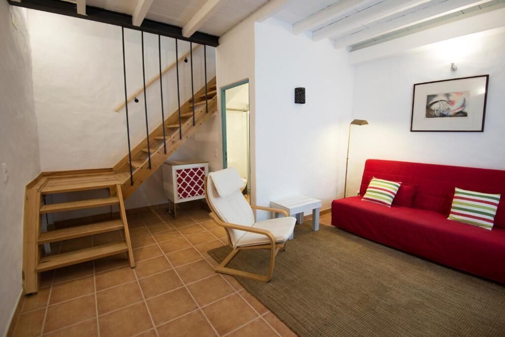 A staircase with wooden steps and black railings, a white chair, a red sofa with striped pillows, and a framed picture on the wall.