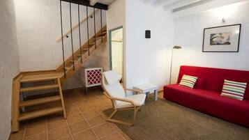 A staircase with wooden steps and black railings, a white chair, a red sofa with striped pillows, and a framed picture on the wall.