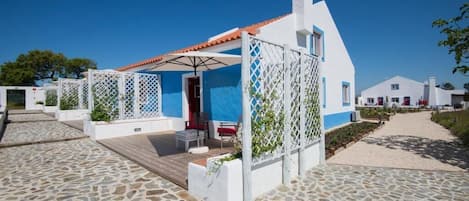 A white building with a blue facade, a tiled roof, and a wooden deck.